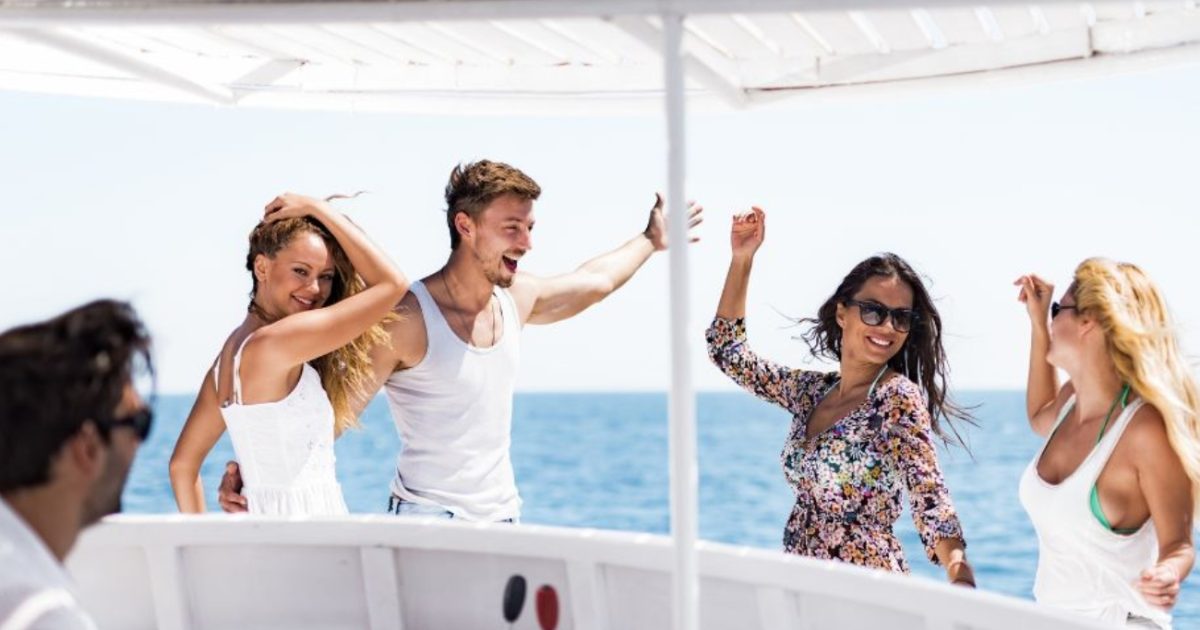 Group of people dancing and enjoying a boat party on the ocean under a shaded deck